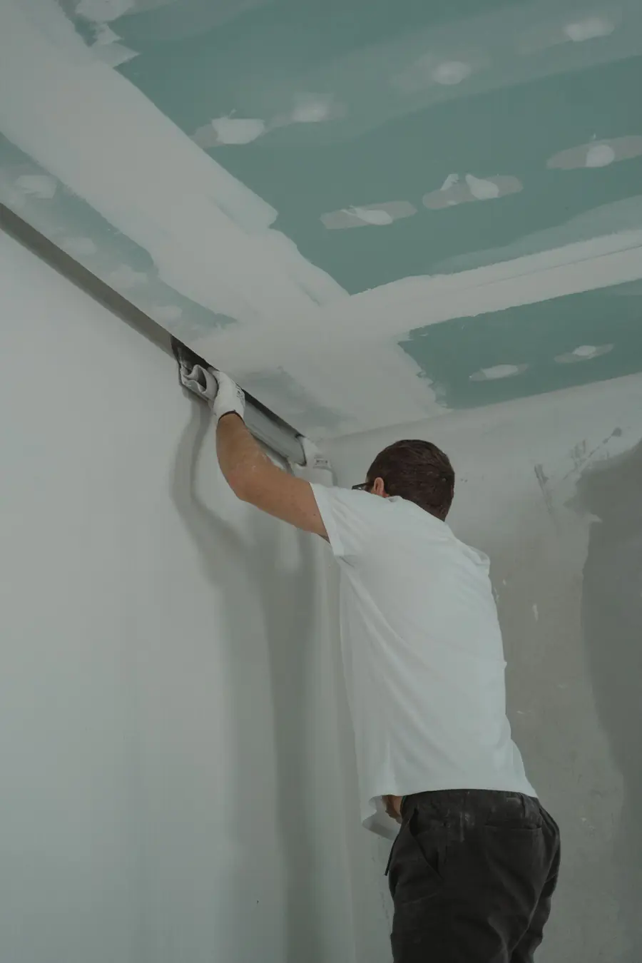 Worker finishing new drywall on a ceiling after the old board was removed